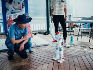 Robot dancing on ground with man crouching to the left and watching